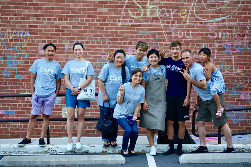 A group of CAFE volunteers standing in front of a chalk art wall.