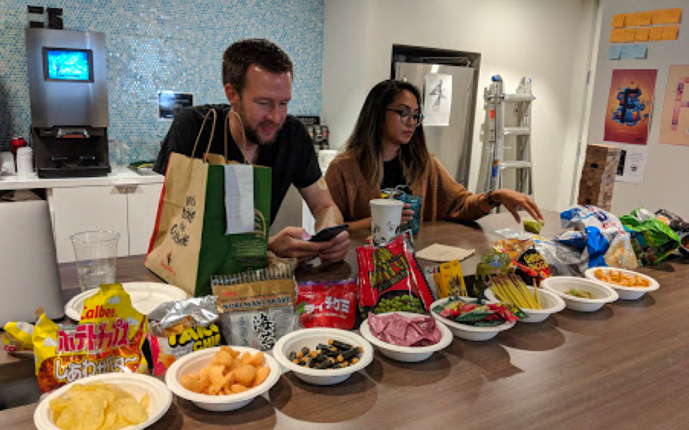 A white man and a Filipino woman setting up behind a row of Korean snacks.
