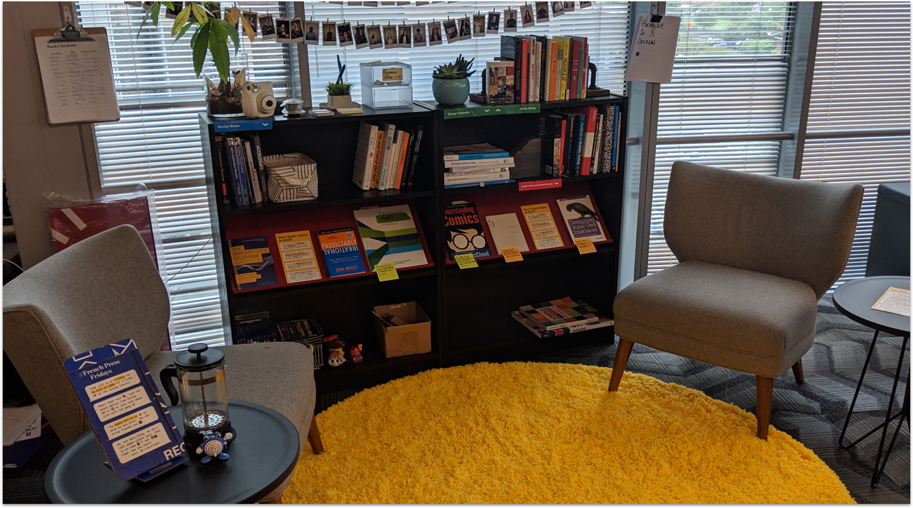 Two black bookshelves on top of a yellow rug with small grey chairs.