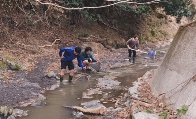 Three people squatting over a rocky creek with bamboo fishing nets. My brother and sister in law are wearing waterproof boots. I'm in crocs.
